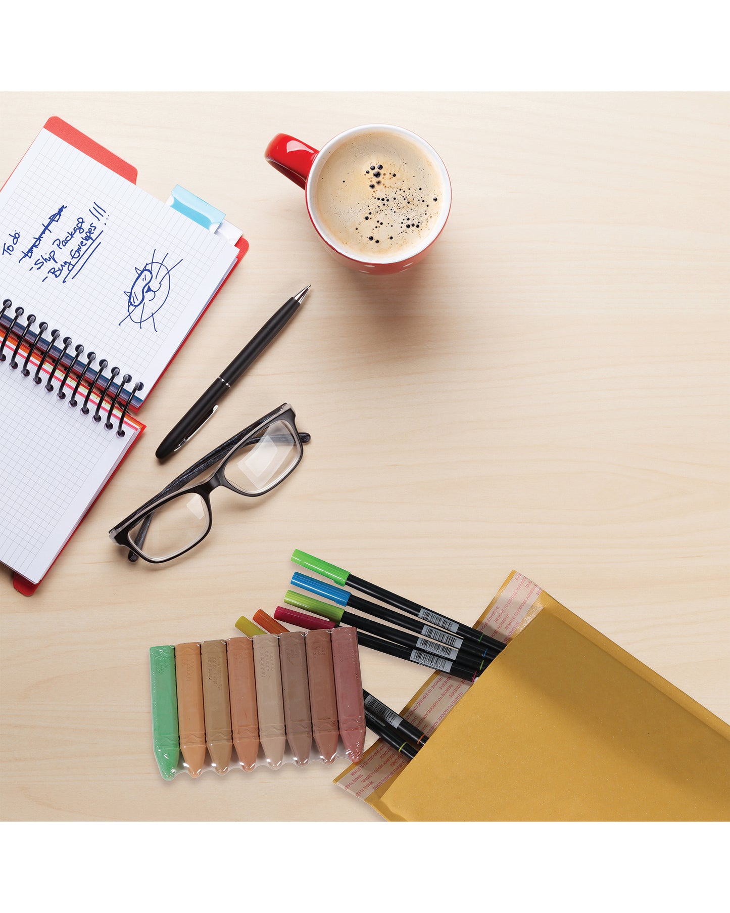 jiffylite mailers displayed with art supplies on a desktop with a notebook, pen, glasses, and cup of coffee